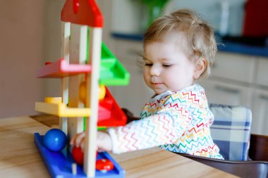 Küçük kız evde ya da çocuk odasında eğitici oyuncaklarla oynuyor. Mutlu sağlıklı çocuk renkli tahta top pisti ile eğleniyor. Çocuk top tutmayı ve yuvarlanmayı öğreniyor. Motorik eğitim