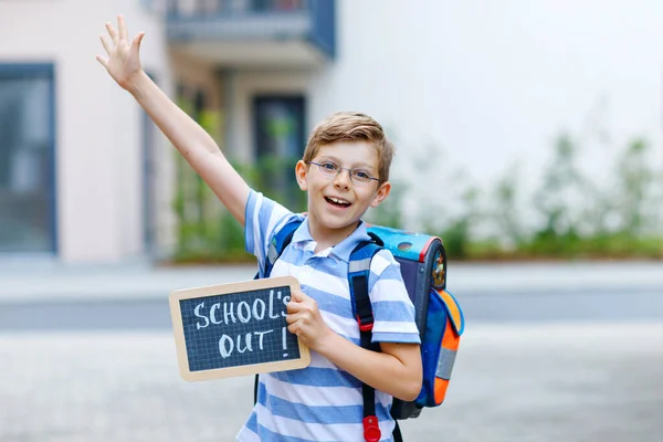 Happy little kid boy with backpack or satchel. Schoolkid on the way to school. Healthy adorable child outdoors With chalk desk for copyspace. Back to school or schools out