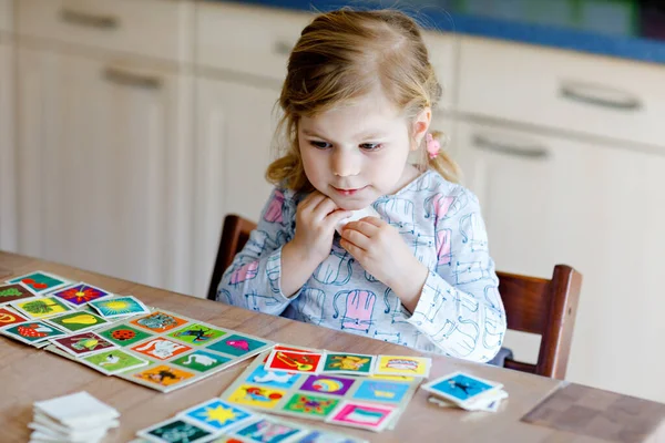 Excited smiling cute toddler girl playing picture card game. Happy healthy child training memory, thinking. Creative indoors leisure and education of kid. Family activity at home