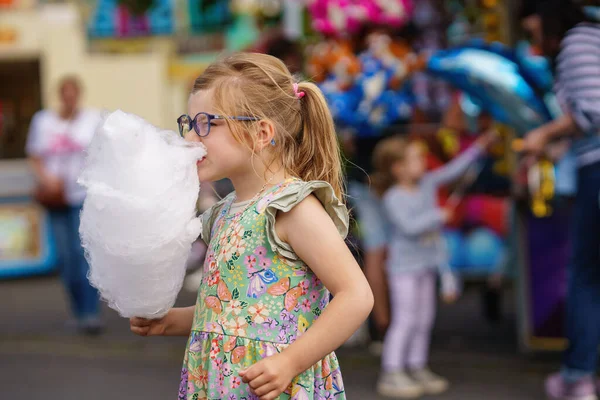 遊園地で綿菓子を食べる愛らしい少女 夏の晴れた日に屋外で眼鏡と大きなキャンディーフロスを持つ幸せな就学前の子供 — ストック写真