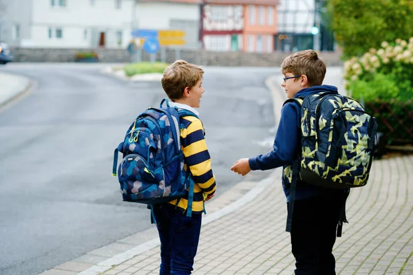 Two kid boys with backpack or satchel. Schoolkids on the way to school. Healthy smiling children, brothers and best friends outdoors on the street leaving home. Back to school. Happy siblings