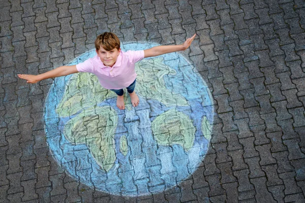 Little school boy with earth globe painting with colorful chalks on ground. Positive kid child. Happy earth day concept. Creation of children for saving world, environment and ecology