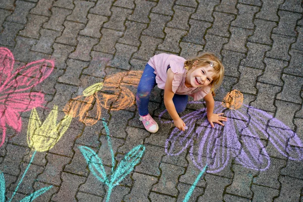 裏庭の地面にカラフルなチョークの花で小さな就学前の女の子の絵 積極的な幸せな幼児の子供はアスファルトの上に絵を描くと作成します 夏の創造的な屋外の子供の活動 — ストック写真