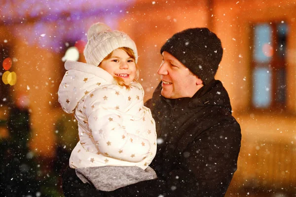 Little preschool girl sitting on shoulder of father on Christmas market in Germany. Happy toddler child and man walking on the streets of German festive city. Family, bonding, love. Family xmas time