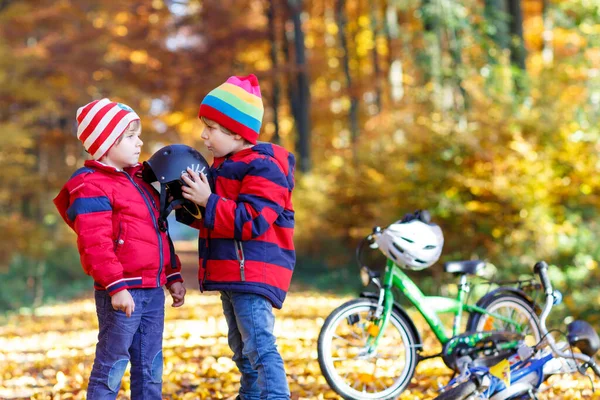 2人の小さな男の子 秋の森の中の親友 弟は若い子供が自然の中で晴れた秋の日にサイクリングする前に安全なヘルメットを置くのを助けます 安全性 スポーツ 子供の概念を持つレジャー — ストック写真