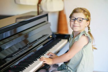Oturma odasında piyano çalan güzel bir anaokulu kızı. Gözlüklü sevimli anaokulu çocuğu müzik aleti çalmayı öğrenirken eğleniyor. Çocuklar için erken müzik eğitimi.