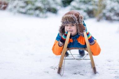 Küçük çocuk kar yağışı sırasında kızak sürmekten hoşlanıyor. Eski model kızakla gezen mutlu anaokulu çocuğu. Çocuk dışarıda karla oynuyor. Kışın aile Noel tatili için aktif eğlence.