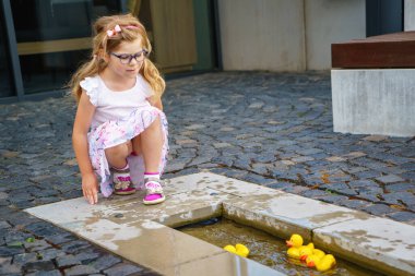 Adorable little preschool girl playing on playground with steam with yellow rubber ducks. Cute child having fun. Active leisure with kids
