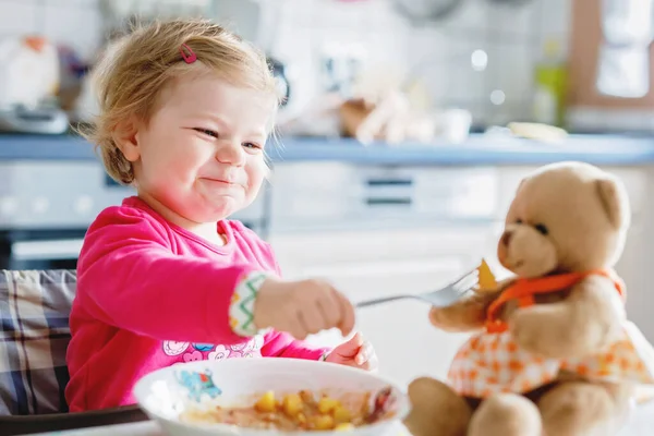 かわいい赤ちゃん女の子フォーク野菜やパスタを食べるします 餌と開発コンセプト かわいい幼児 スプーンでハイチェアに座っていると ひとりでに食べ方を学ぶ娘 — ストック写真