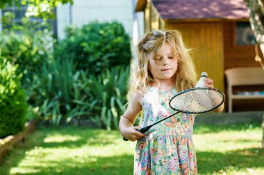 Cute little girl playing badminton outdoors on warm and sunny summer day. Preschool child having fun with outdoor activity and sports.