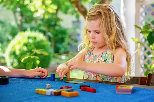Little preschool girl playing board game with colorful bricks. Happy child build tower of wooden blocks, developing fine motor skills, home joint games. Leisure activities for children at home