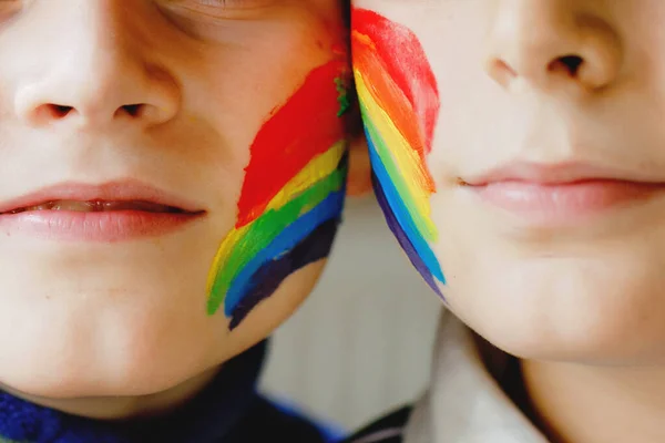 Two kid boys with painted rainbow with colorful colors on face during pandemic coronavirus quarantine. Children make and paint rainbows around the world. Siblings, best friends.