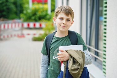 Happy preteen kid boy with backpack or satchel. Schoolkid in on the way to elementary or middle school on warm sunny summer day. Healthy child outdoors on the street in the city