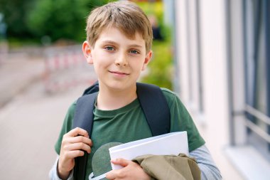 Happy preteen kid boy with backpack or satchel. Schoolkid in on the way to elementary or middle school on warm sunny summer day. Healthy child outdoors on the street in the city