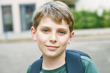 Happy preteen kid boy with backpack or satchel. Schoolkid in on the way to elementary or middle school on warm sunny summer day. Healthy child outdoors on the street in the city