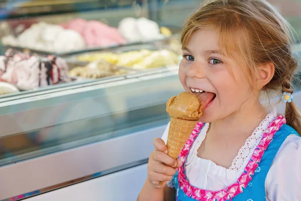 Little preschool girl eating sweet ice cream in waffle cone on sunny summer day. Happy toddler child eat icecream dessert. Sweet food on hot warm summertime days.