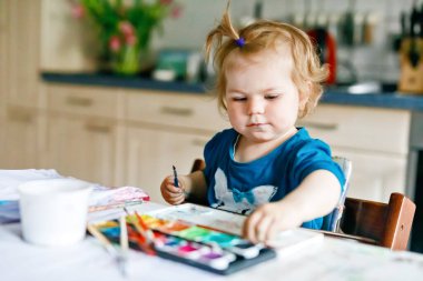 Kağıt üzerinde sulu boyayla resim yapan tatlı, mutlu küçük bir kız. Bebek farklı beceriler, yaratıcı eğlence ve küçük çocuklar için etkinlik öğreniyor.