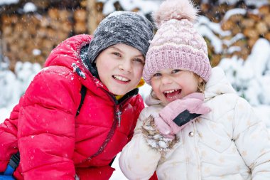Portrait of little preschool girl and school boy playing with snow in winter. Brother and cute sister together during snowing Happy smiling children. Outdoors activity for kids
