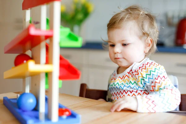 Küçük kız evde ya da çocuk odasında eğitici oyuncaklarla oynuyor. Mutlu sağlıklı çocuk renkli tahta top pisti ile eğleniyor. Çocuk top tutmayı ve yuvarlanmayı öğreniyor. Motorik eğitim