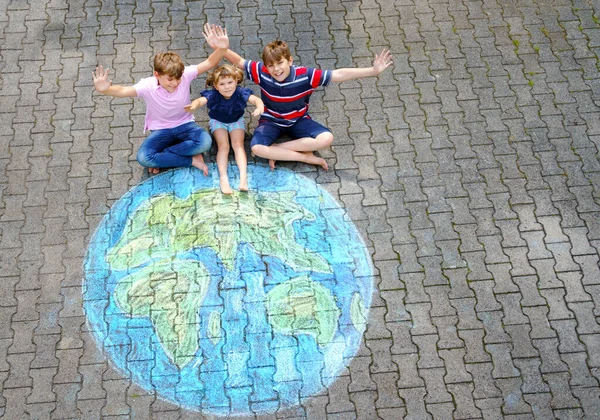 Little preschool girl and two school kids boys with earth globe painting with colorful chalks on ground. Happy earth day concept. Creation of children for saving world, environment and ecology
