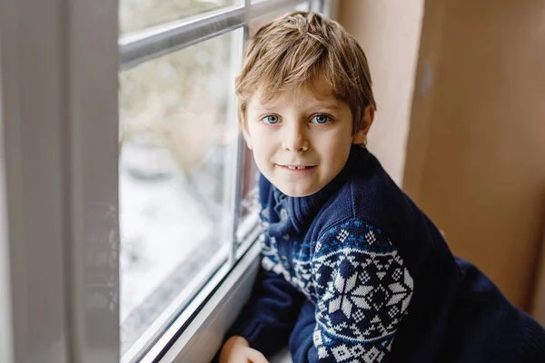 快乐可爱的小男孩坐在窗边 在圣诞节的那天或早上看着外面的雪 笑着健康的孩子着迷于观察降雪和大雪 — 图库照片