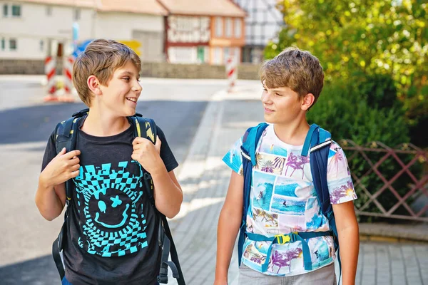 リュックかサッチェルを持った2人の少年 学校に行く途中の子供たち 健康的な笑顔の子供たちは 兄弟や親友屋外の通りに家を出る 学校に戻る 幸せな兄弟たち — ストック写真