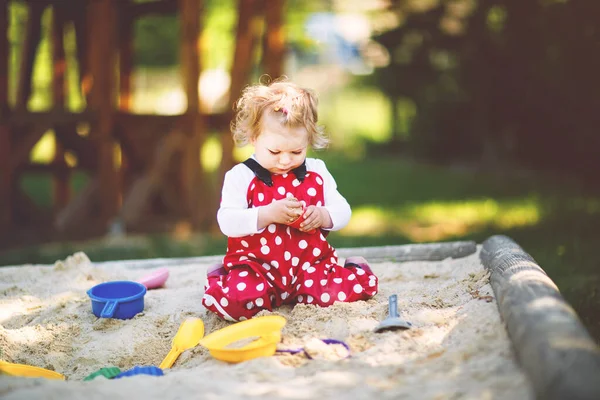 可爱的幼儿女孩在户外操场上玩沙子 美丽的宝宝穿着红胶裤 在阳光灿烂温暖的夏日里玩得很开心 带着五彩缤纷的沙玩具的孩子健康活泼的宝宝在户外玩游戏 — 图库照片