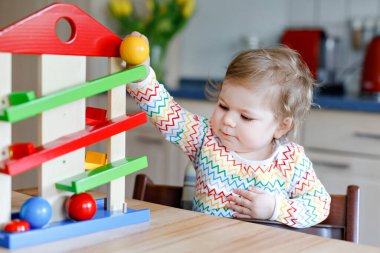 Küçük kız evde ya da çocuk odasında eğitici oyuncaklarla oynuyor. Mutlu sağlıklı çocuk renkli tahta top pisti ile eğleniyor. Çocuk top tutmayı ve yuvarlanmayı öğreniyor. Motorik eğitim