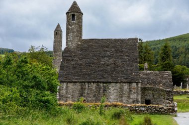 Taş yuvarlak kule ve bir manastır yerleşim bazı kalıntıları aslında Glendalough vadisinde 6 yüzyılda inşa, County Wicklow, İrlanda güneşli bir günde.
