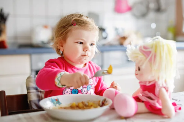 かわいい赤ちゃん女の子フォーク野菜やパスタを食べるします 餌と開発コンセプト かわいい幼児 スプーンでハイチェアに座っていると ひとりでに食べ方を学ぶ娘 — ストック写真