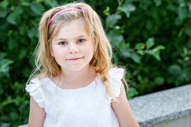 Dışarıda gülümseyen küçük kızın portresi. Sarı saçlı küçük çocuk kameraya bakıyor ve gülümsüyor. Mutlu sağlıklı çocuk dışarıda eğleniyor ve oyun oynuyor.