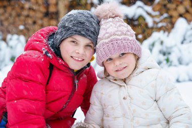 Portrait of little preschool girl and school boy playing with snow in winter. Brother and cute sister together during snowing Happy smiling children. Outdoors activity for kids