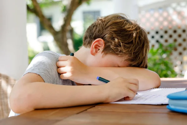 Hard-working sad school kid boy making homework during quarantine time from corona pandemic disease. Upset tired child on home schooling in coronavirus covid time, schools closed