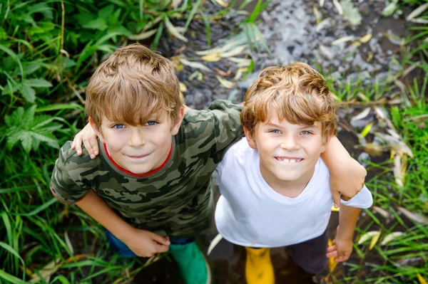 2人の幸せな小さな学校の子供たち 面白い兄弟は一緒にゴム製のブーツで川の中を歩いて楽しんでいます 健康な兄弟と親友の家族の肖像画 — ストック写真