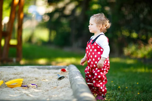 屋外の遊び場で砂の中で遊んでいるかわいい幼児の女の子 晴れた暖かい夏の日に楽しんでいる赤いガムのズボンの中の美しい赤ちゃん カラフルな砂のおもちゃを持つ子供 健康な活動的な赤ちゃんの屋外で遊ぶゲーム — ストック写真