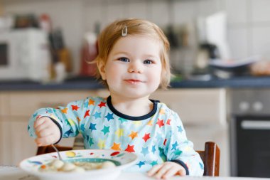 Sevimli bebek kaşık sebze çorbası içiyor. Yemek, çocuk, beslenme ve gelişim konsepti. Sevimli bebek, kaşıklı kız sandalyede oturuyor ve kendi kendine yemek yemeyi öğreniyor.