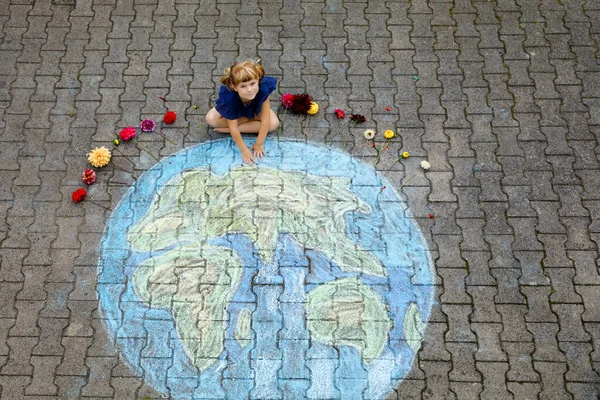 Little preschool girl with flowers and earth globe painting with colorful chalks on ground. Positive toddler child. Happy earth day concept. Creation of children for saving world, environment ecology