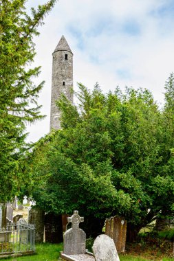 Taş yuvarlak kule ve bir manastır yerleşim bazı kalıntıları aslında Glendalough vadisinde 6 yüzyılda inşa, County Wicklow, İrlanda güneşli bir günde.
