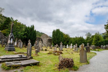 Taş yuvarlak kule ve bir manastır yerleşim bazı kalıntıları aslında Glendalough vadisinde 6 yüzyılda inşa, County Wicklow, İrlanda güneşli bir günde.