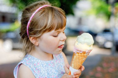 Güneşli yaz gününde krep külahında dondurma yiyen küçük bir anaokulu kızı. Mutlu çocuk dondurma tatlısı yesin. Sıcak yaz günlerinde tatlı yiyecekler. Parlak ışık, renkli dondurma..