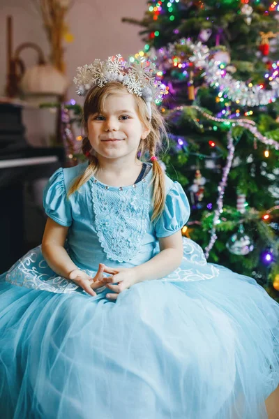圣诞节的早上或晚上 小矮小的小女孩穿着公主的衣服坐在那里 背景上挂着圣诞树和灯 健康快乐的孩子庆祝家人的传统节日 等待礼物 — 图库照片