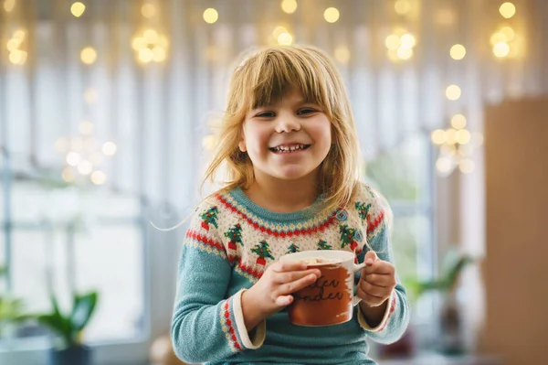 学龄前小女孩拿着一杯热巧克力和玛哈蜜糖 快乐的孩子在冬天开着圣诞灯 在窗边喝甜可可 舒适的圣诞家庭庆祝活动 — 图库照片