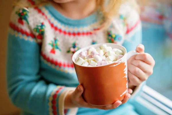 小学龄前女孩拿着一杯热巧克力和玛哈蜜糖的衣服 快乐的孩子在冬天开着圣诞灯 在窗边喝甜可可 舒适的圣诞家庭庆祝活动 — 图库照片
