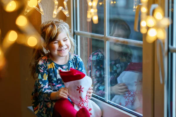学龄前小女孩拿着装有礼物的杯子圣诞老人靴 德语叫Nikolausstiefel 快乐的孩子在冬天开着圣诞灯在窗边等着 舒适的圣诞家庭庆祝活动 — 图库照片