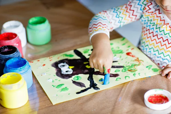 Closeup of little creative toddler girl painting with finger colors an owl bird. Child having fun with drawing at home, in kindergaten or preschool. Games, education and distance learning for kids