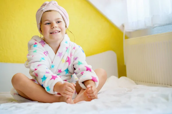 入浴後の就学前の子供 バスローブと頭のタオルをベッドの上に座って着て濡れた巻き毛のかわいい女の子 赤ん坊及び子供のための浴室の繊維 — ストック写真