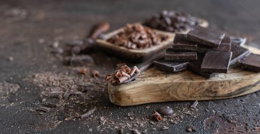 Koyu beton arka planda çikolata parçaları, damlalar ve kırıntılar. Farklı çikolata çeşitleri olan bir arka plan..