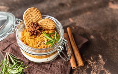 Cam kavanozda, biberiye, anason ve koyu arkaplanla süslenmiş kurabiye parçalı kremalı tatlı. Peynirli kek, çerez ya da puding yok..