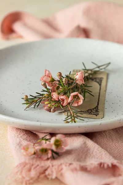 Romantisch, Hochzeit oder Frühling Tischdekoration. Leerer Teller mit Karte und kleinen rosa Blümchen, heller Hintergrund. Nahaufnahme. — Stockfoto