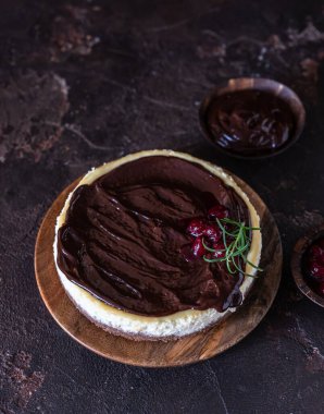 Çikolata soslu kremalı cheesecake ve koyu beton arka planda biberiyeyle süslenmiş kiraz..